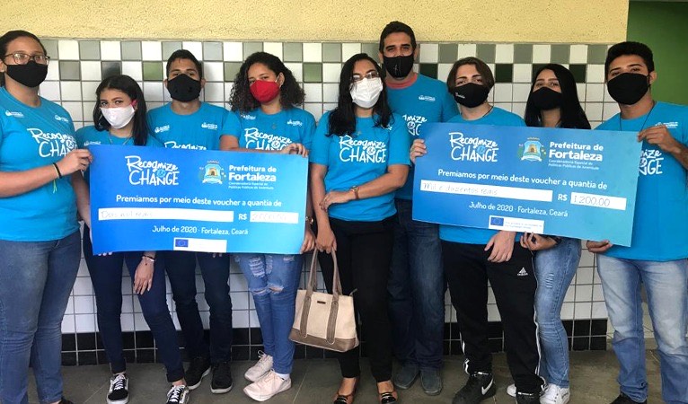 grupo de jovens posa para a foto, seguran cheques simbólicos